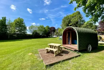 Wooden painted camping pods with deck areas and picnic benches