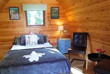 Large camping pod interior with a double bed, heating and camp kitchen