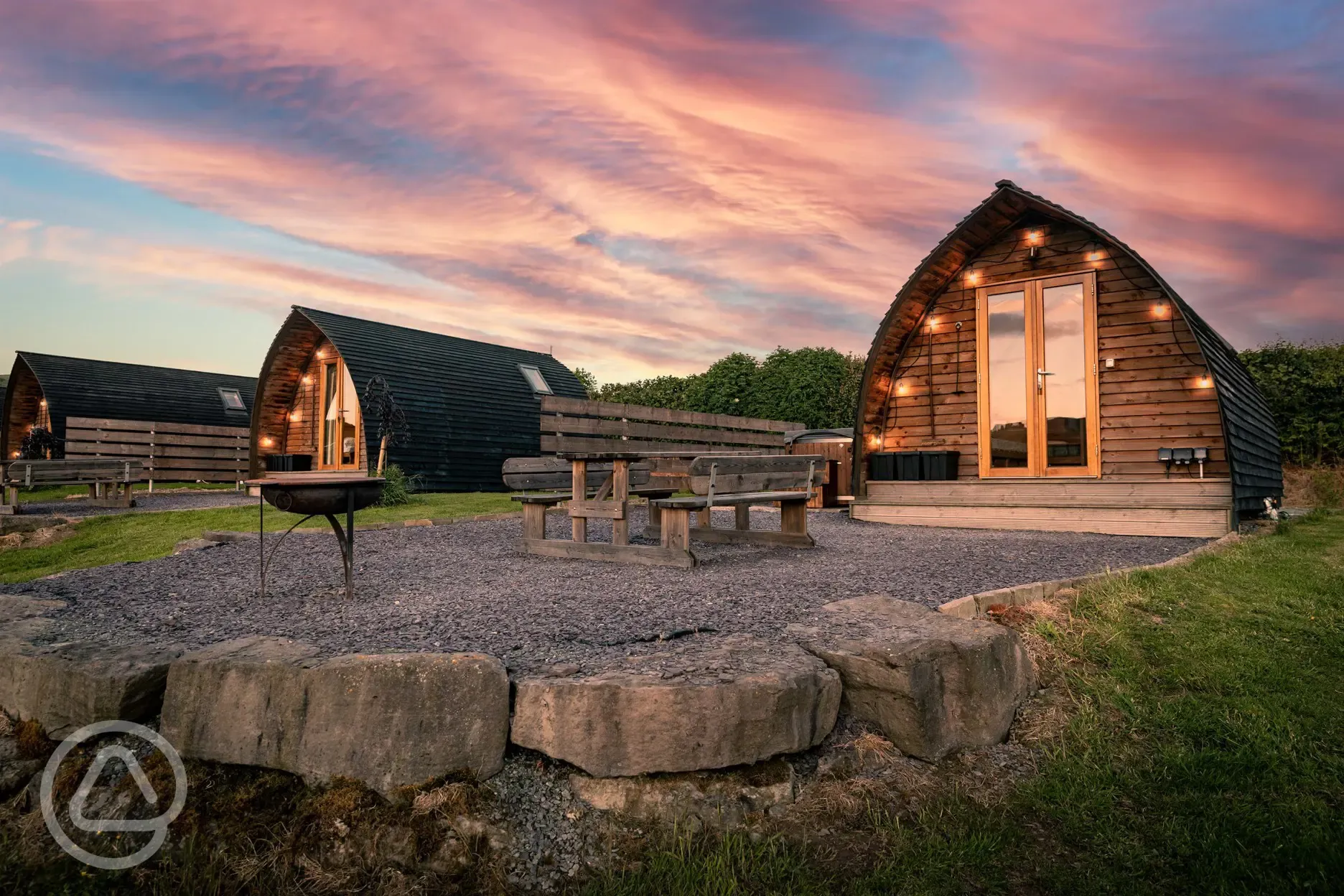 Glamping pods at dusk with outdoor lighting, fire pits and picnic benches
