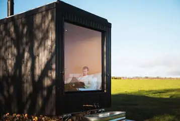 Hare glamping cabin with an outdoor bath and a large glass window by the bed